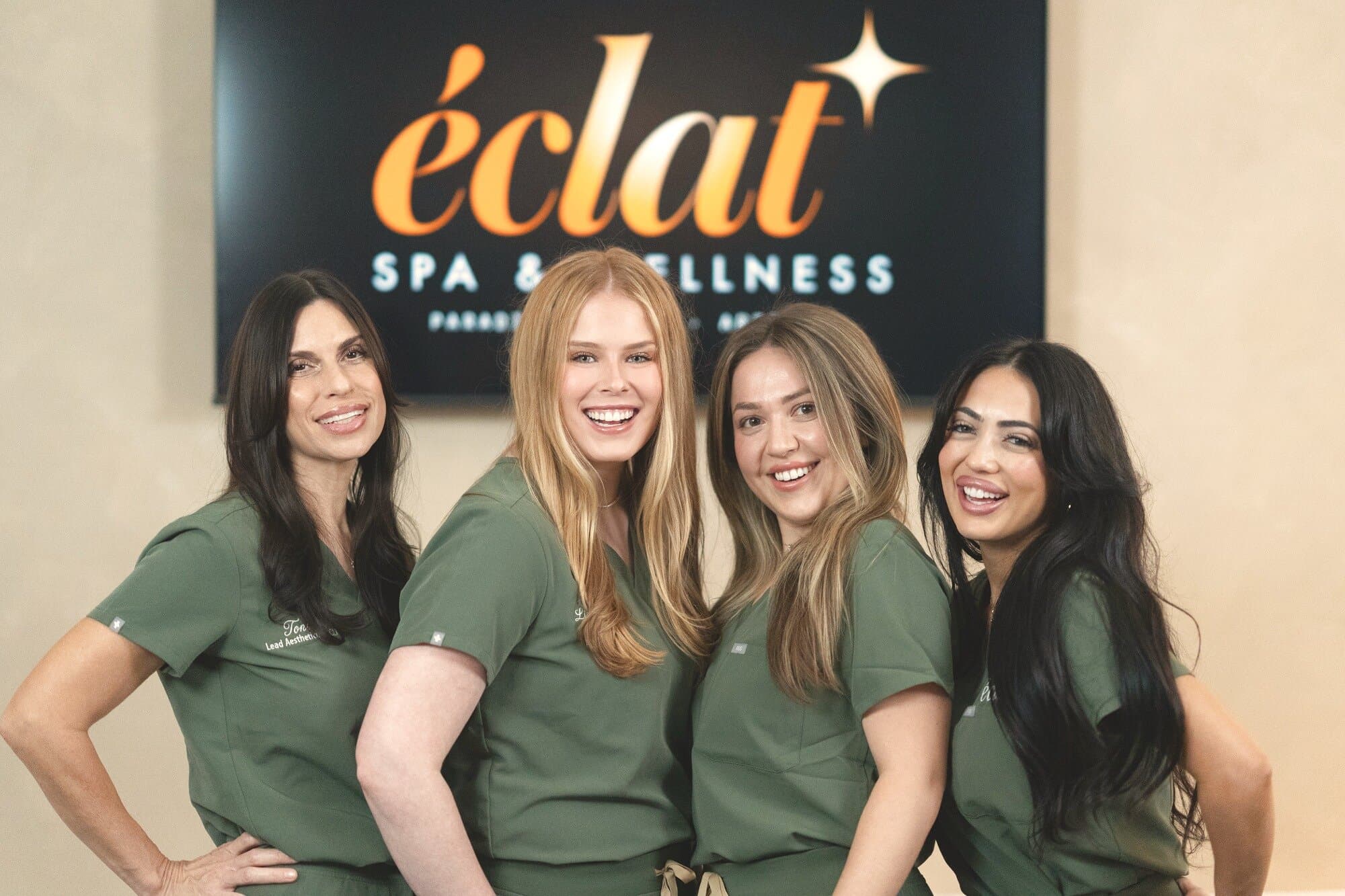 The team at éclat Spa & Wellness, in olive scrubs beside the lobby sign in North Phoenix