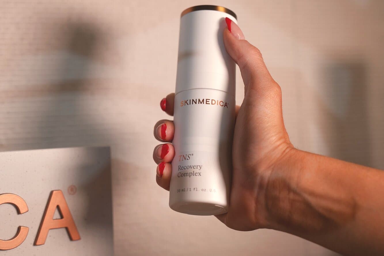A hand holding a SkinMedica bottle beside its box