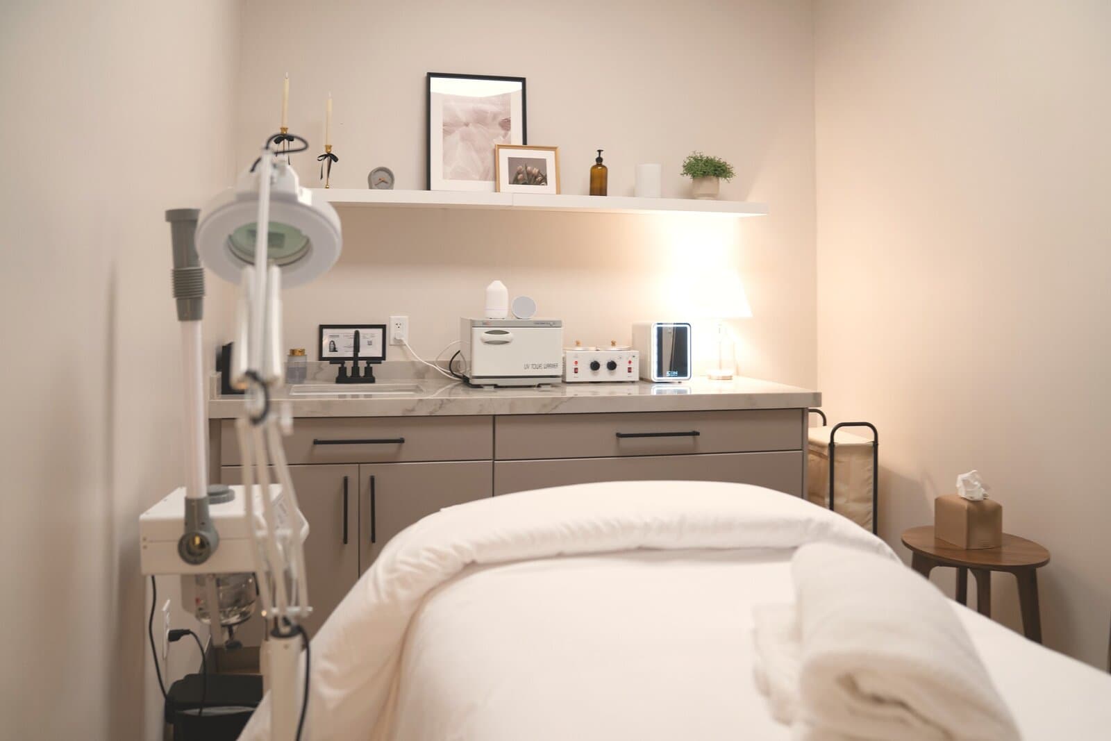 A treatment room at éclat, bed made up in white beside the wall lamp and shelf