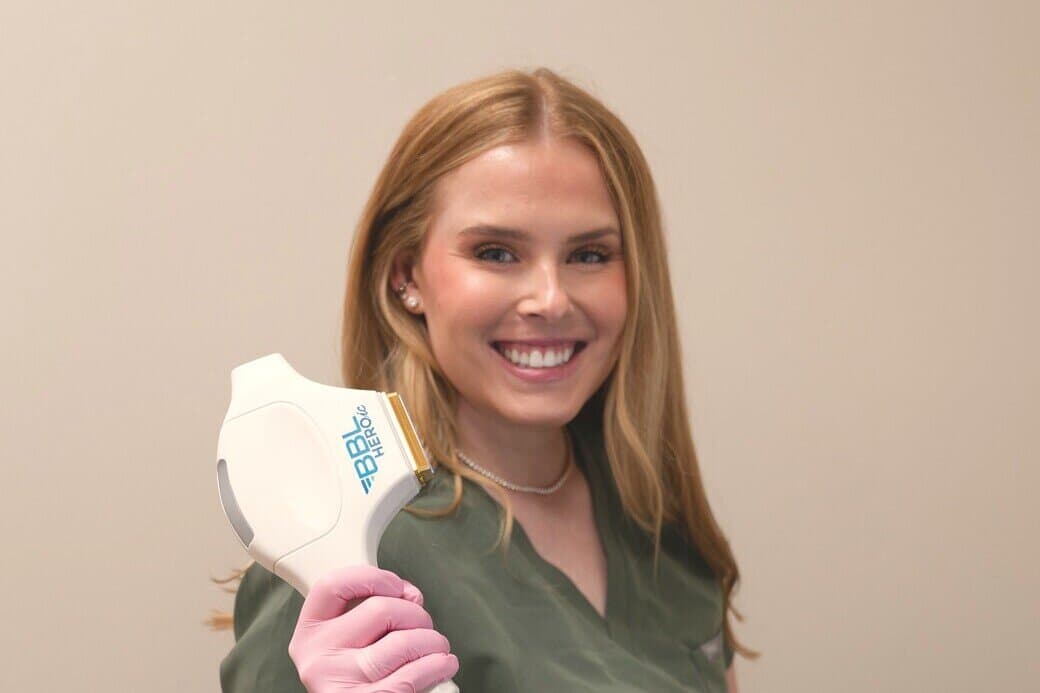 An aesthetician smiling beside the treatment platform, handpiece in hand